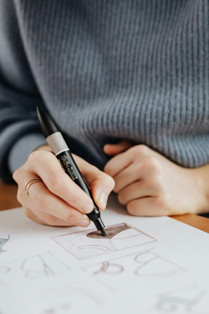 Woman artist wearing sweater drawing with marker on paper, focus on hand and sketch.
